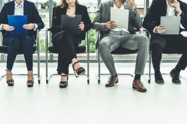 Businesswomen and businessmen holding resume CV folder while waiting on chairs in office for job interview. Corporate business and human resources concept.