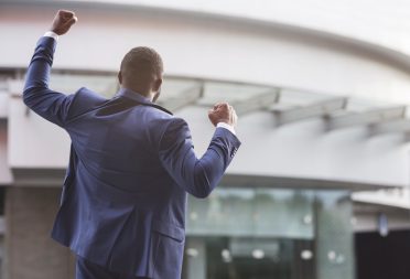 African american job seeker celebrating successful interview raising fists against business center, rear view with copy space